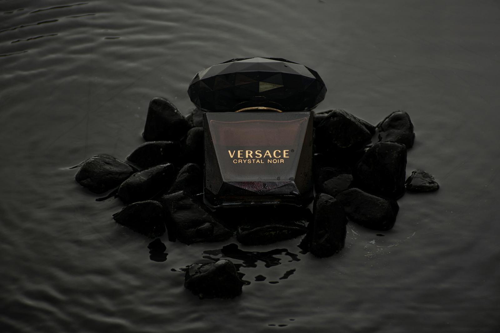 Elegant product shot of Versace Crystal Noir perfume on black stones.